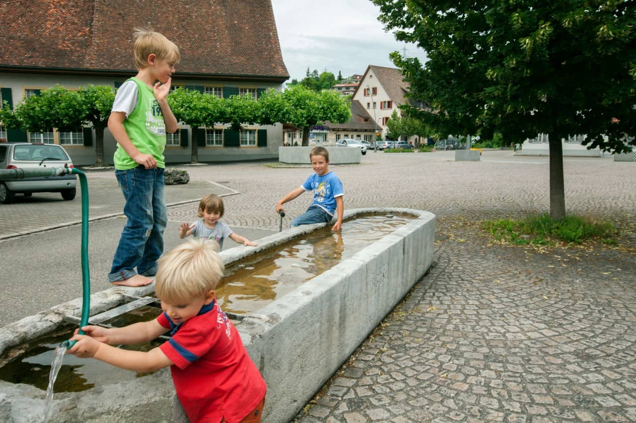 Kinder spielen am Brunnen auf dem Dorfplatz.