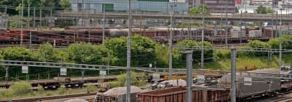 Foto des Rangierbahnhofs Limmattal mit Güterzügen im Vordergrund und dem Industriegebiet von Spreitenbach im Hintergrund.