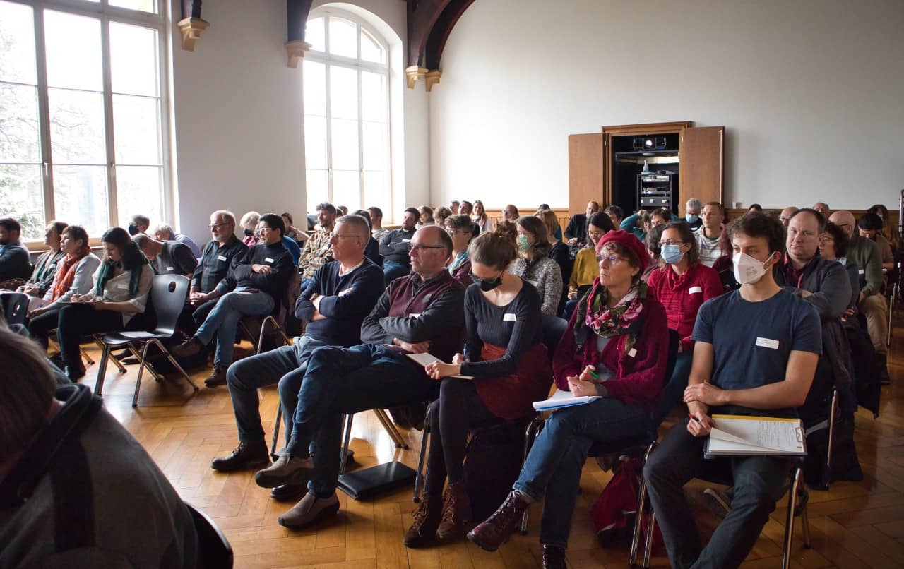 Mehrere Personen sitzen in einem Saal und hören einem Vortrag zu.