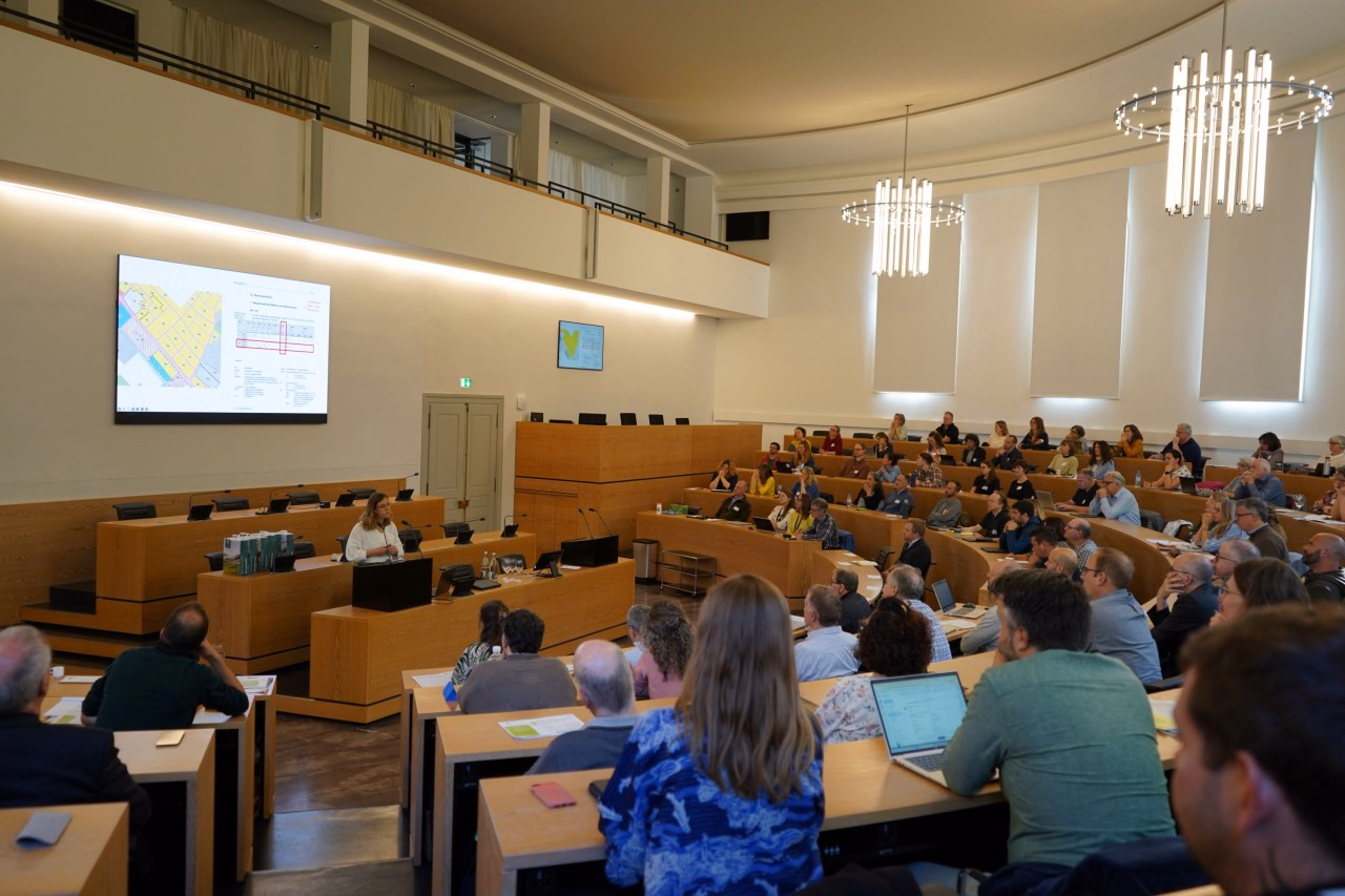 Personen die in einem Saal dem Vortrag von Esther van der Werft zuhören.