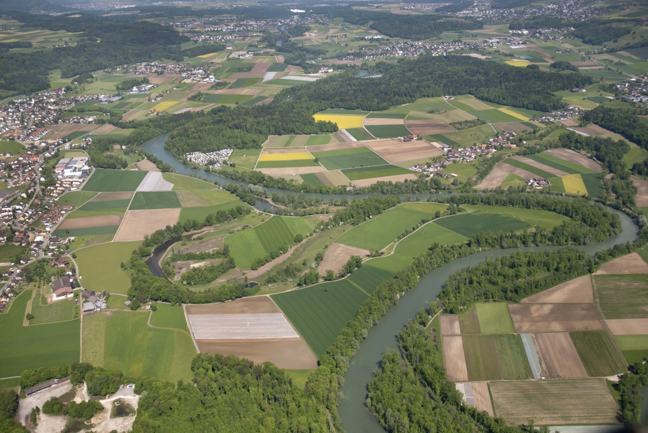 Luftaufnahmen, auf der man die Reuss mit umliegenden Siedlungen, Feldern und Wäldern sieht.