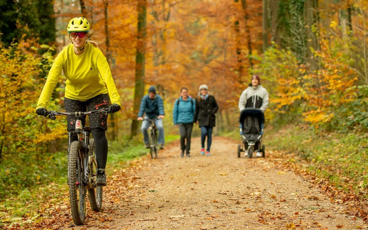 Zwei Velofahrende überholen rücksichtsvoll eine Gruppe Spaziergänger auf einem Waldweg.