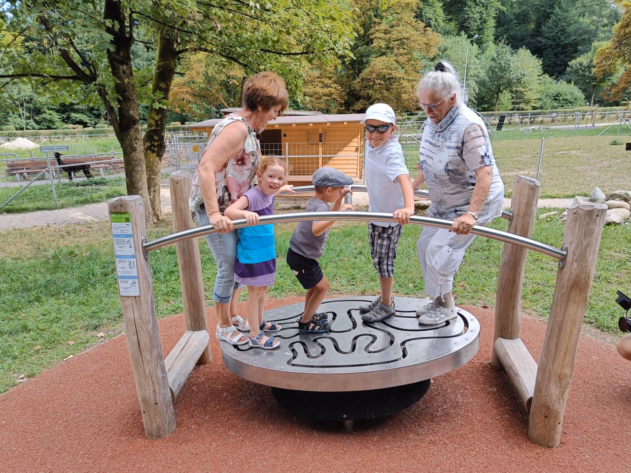 Zwei ältere Frauen stehen mit drei Kindern unterschiedlichen Alters auf einer Wippe.