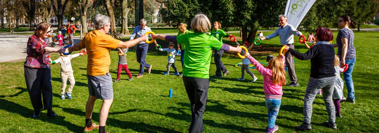 Ältere Personen und Kinder stehen in einem Kreis und halten sich an den Händen.