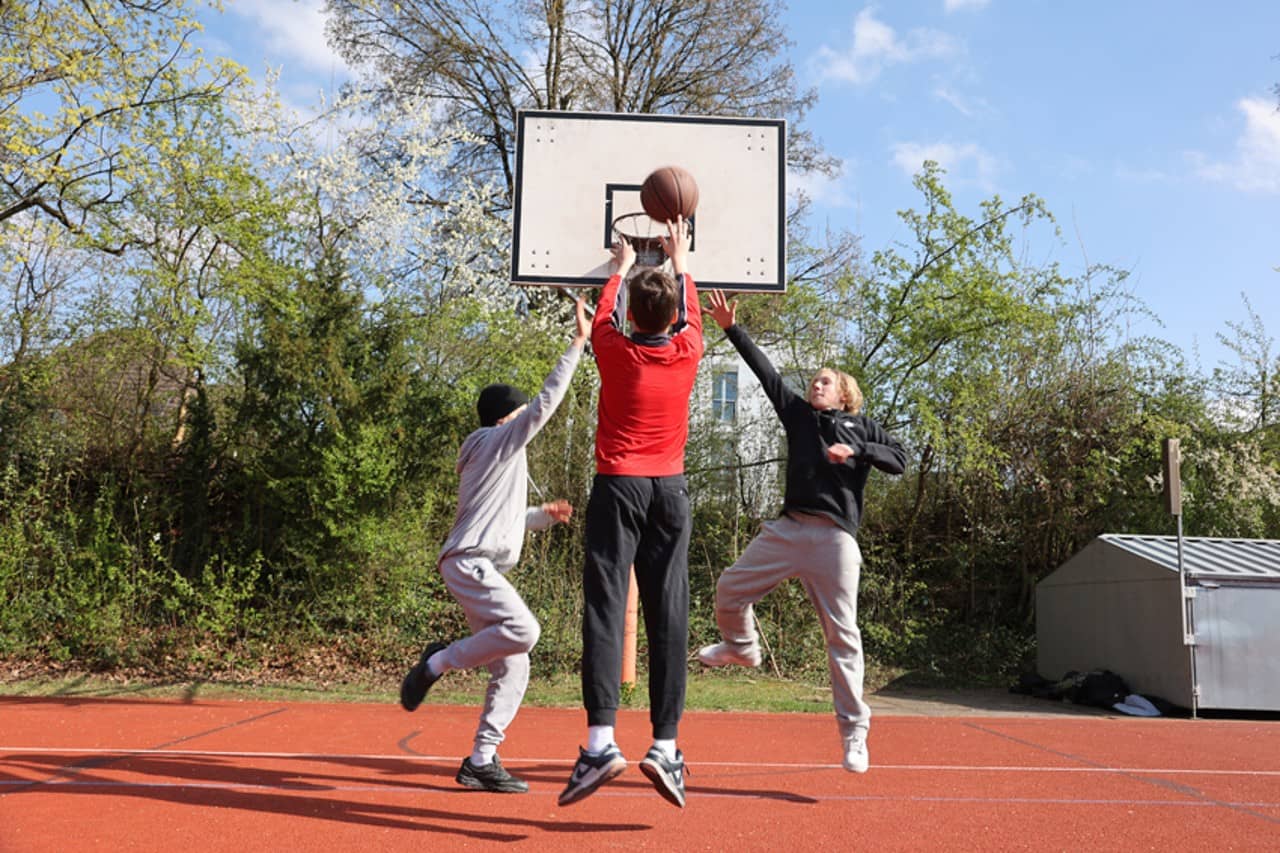 Auf dem Bild sieht man drei Jugendliche, die Basketball spielen.