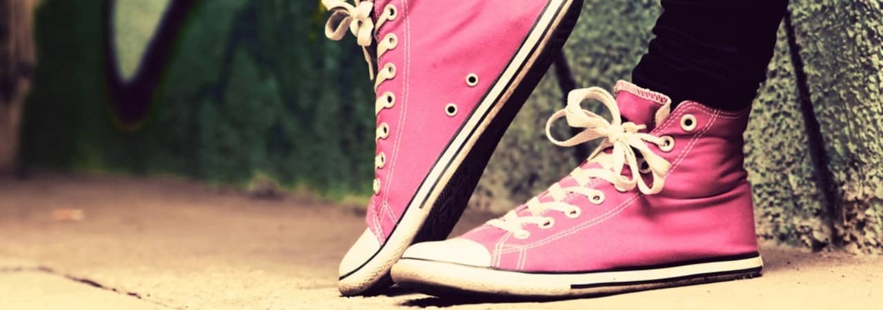 Füsse einer Person in pinken Conversen Schuhen, an Wand mit Graffiti gelehnt. Rechter Fuss auf Zehenspitzen. 