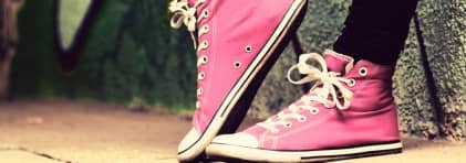 Füsse einer Person in pinken Conversen Schuhen, an Wand mit Graffiti gelehnt. Rechter Fuss auf Zehenspitzen. 
