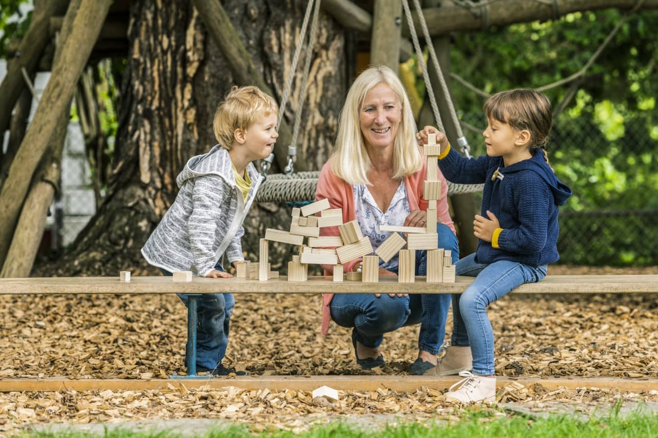 Zwei Kinder spielen und eine Frau schaut zu