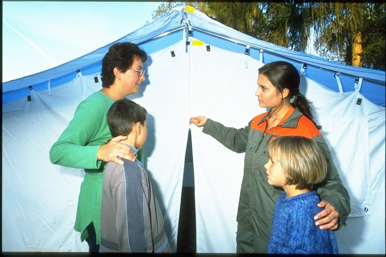 Eine Zivilschutzdienstleistende führt eine Familie in Not in ein Zelt.