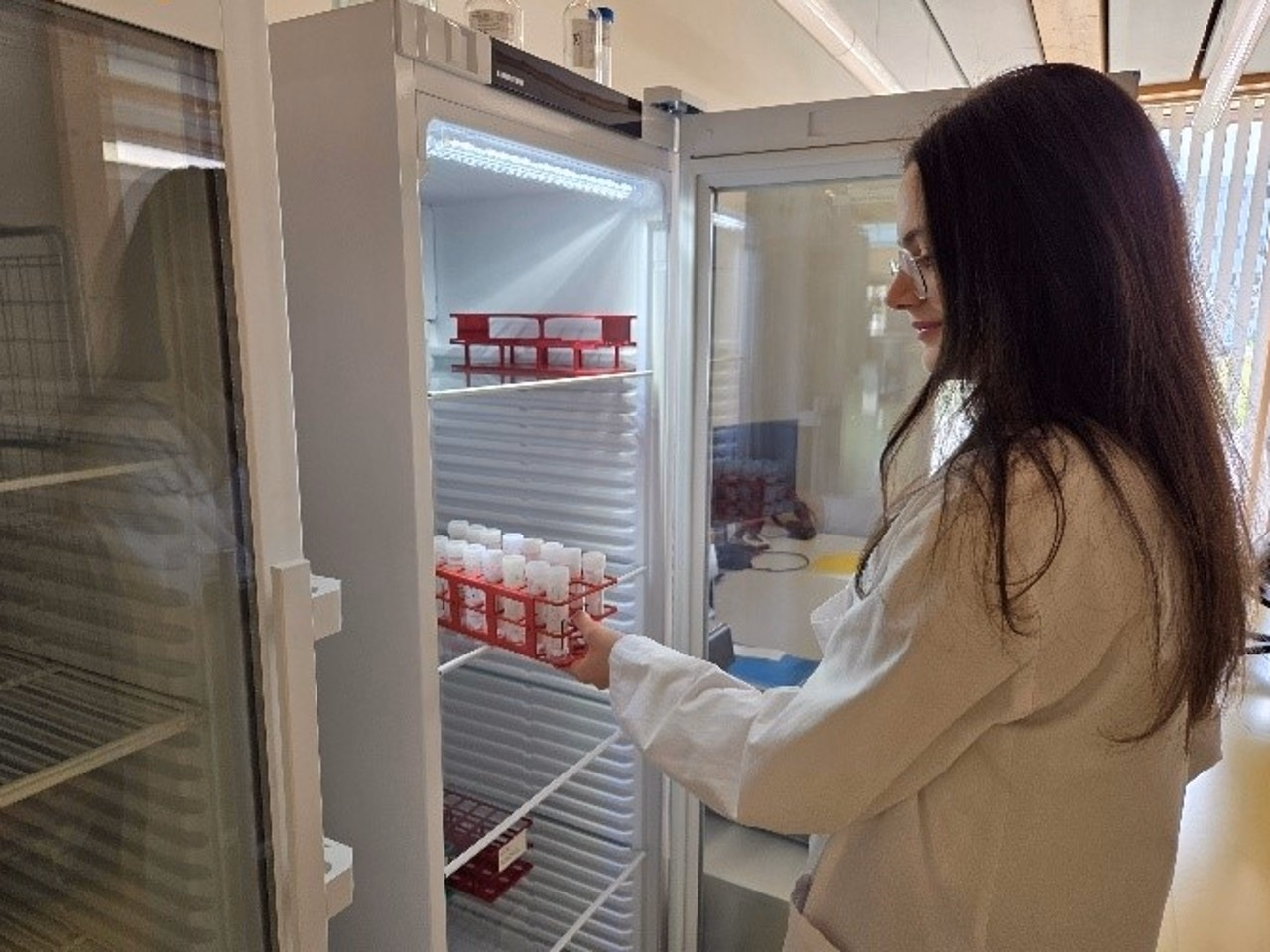 Person steht vor Kühlschrank und hat Gefäss mit Röhrchen in der Hand.