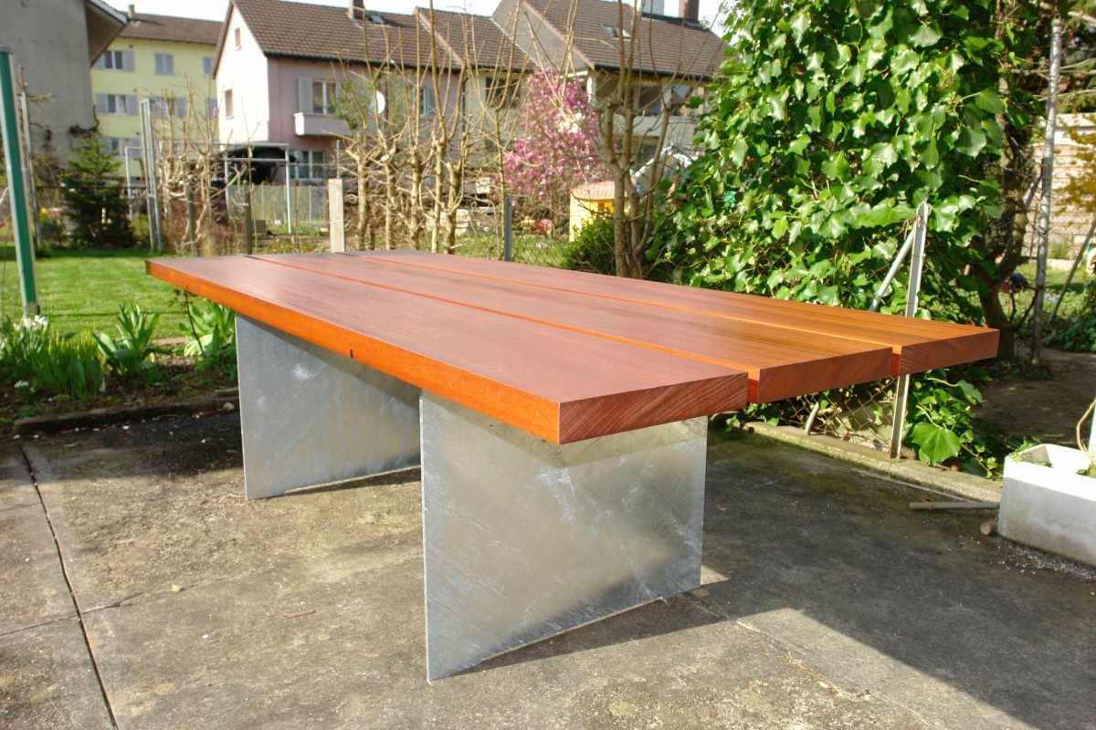 Tisch für den geschützten Aussenbereich mit Tischplatte aus rötlichem Massivholz auf zwei Alusockelplatten