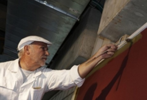 Älterer Maler beim Streichen einer dunkelroten Wand