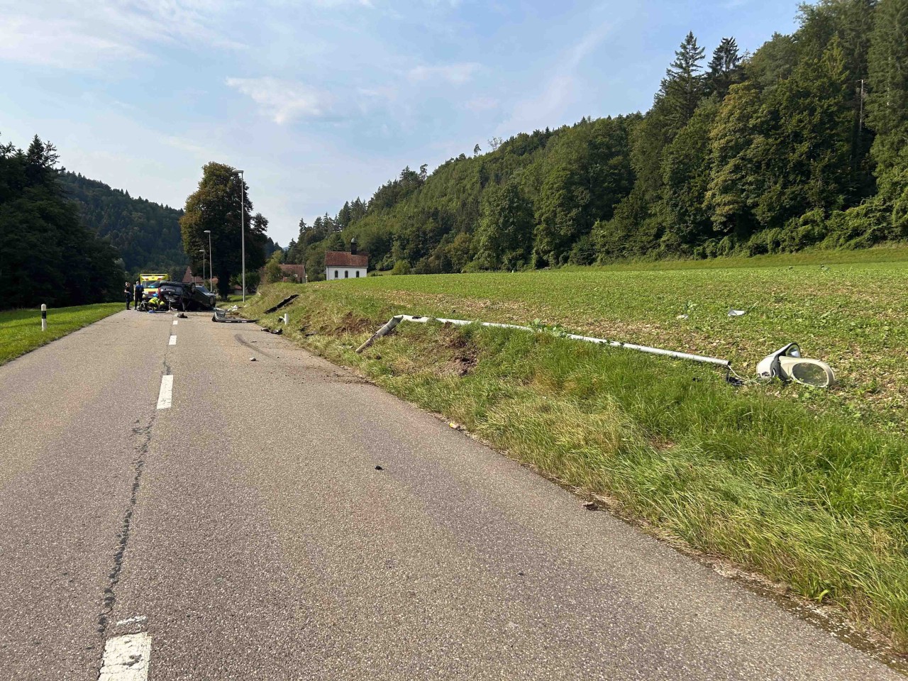 Umgeknickter Kandelaber, weiter vorne Fahrzeug auf dem Dach liegend mittig auf der Strasse.