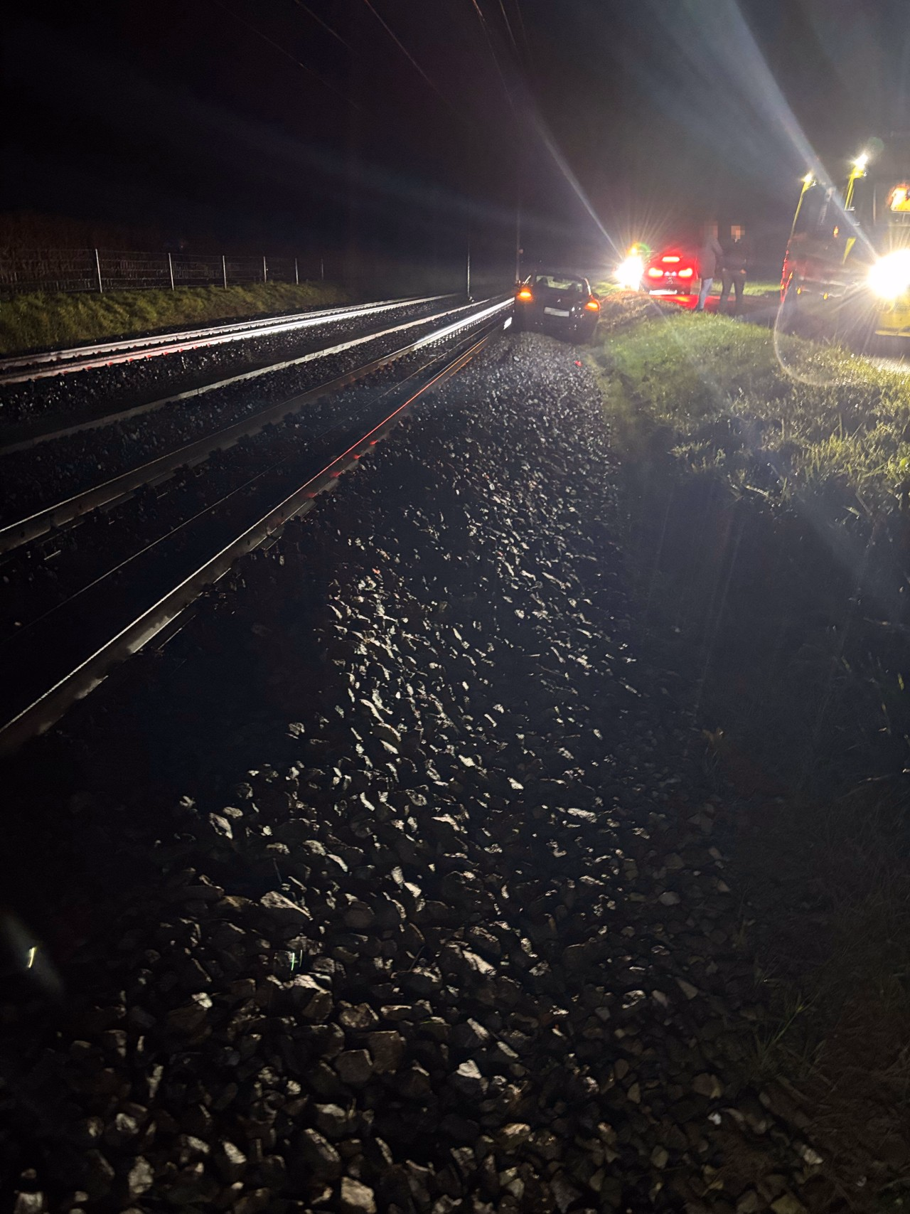 Schwarzes Fahrzeug auf Gleise. Krankenwagen daneben. Zwei Personen auf der Strasse.