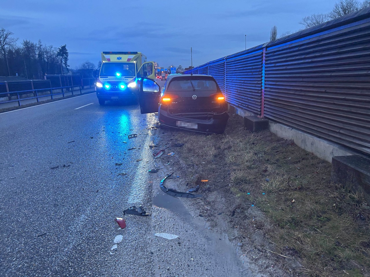 Beschädigtes Fahrzeug mit Ambulanz im Hintergrund.