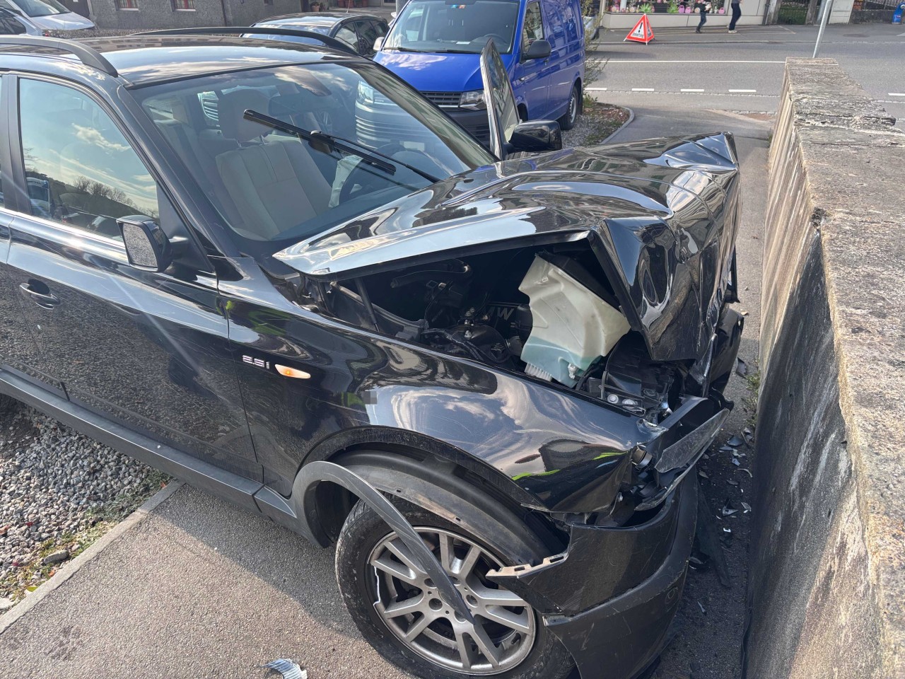 Stark beschädigter, schwarzer BMW, welcher mit einer Mauer kollidiert ist.