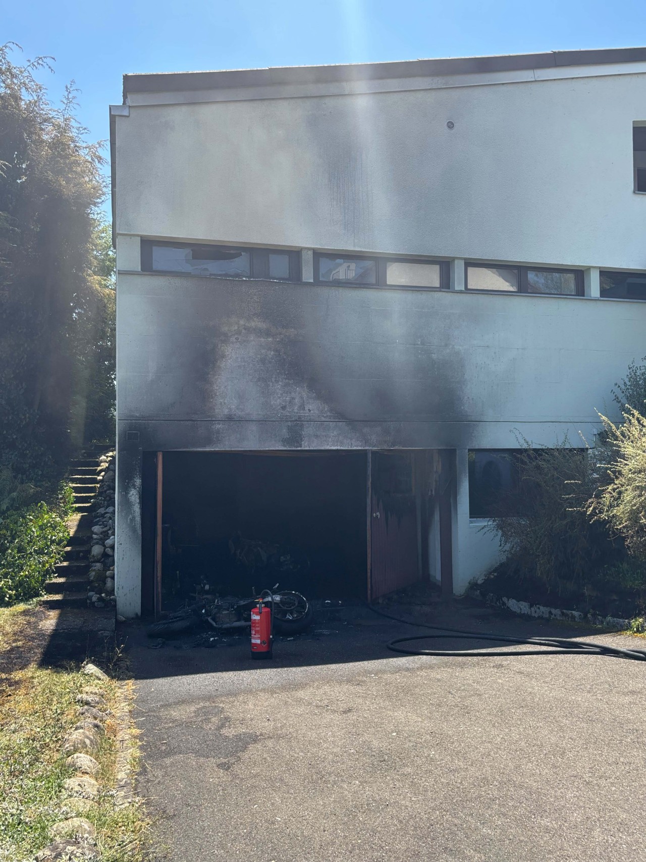 Einfamilienhaus, welches russgeschwärzt ist. Ausgebranntes Motorrad liegt vor der Garage.