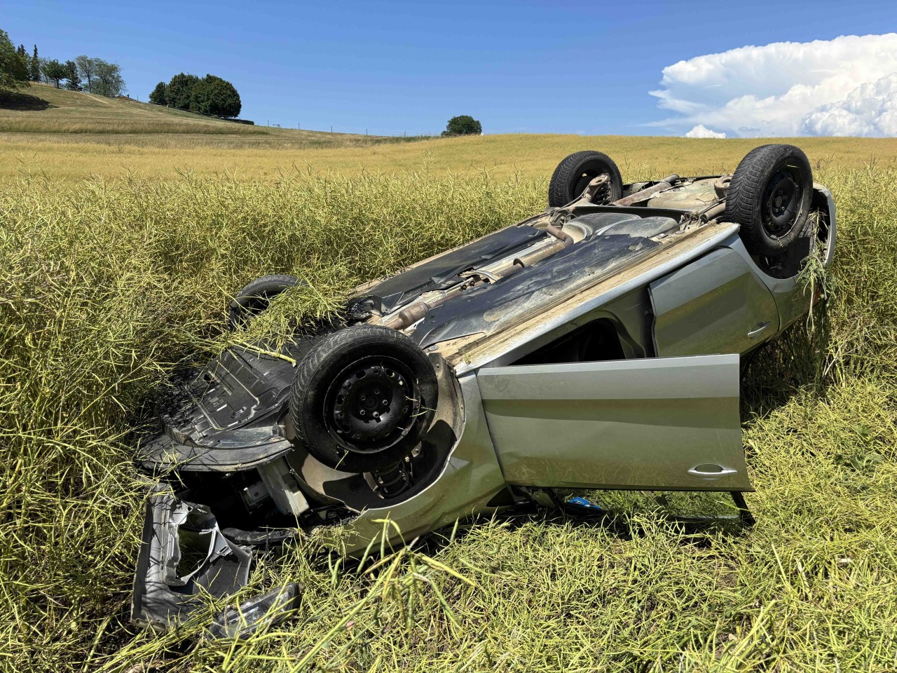 Grauer Kleinwagen, welcher auf dem Dach liegt in einem Feld.