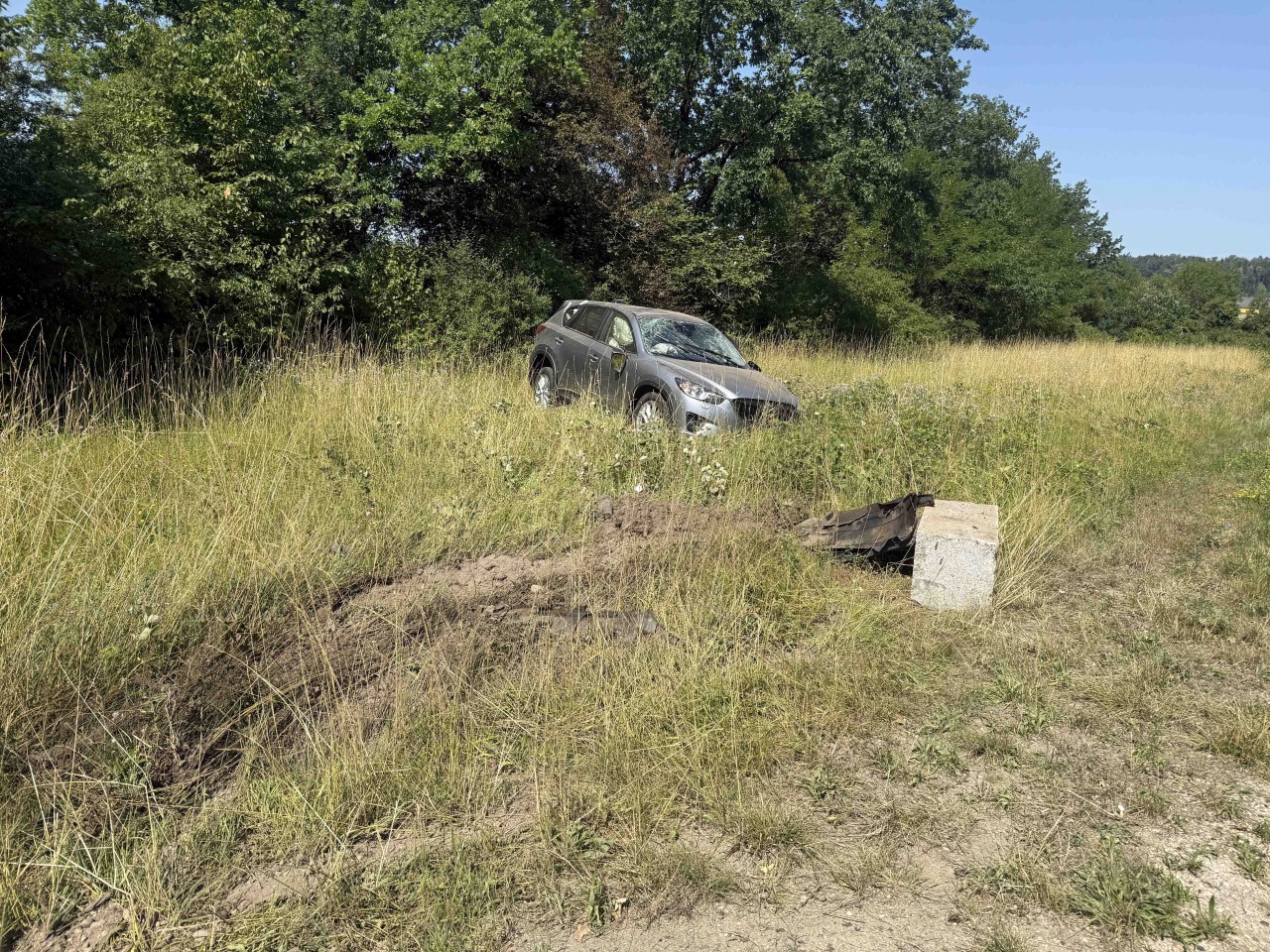 Auto steht beschädigt im Wiesland. Vor dem Auto liegt ein Steinblock.