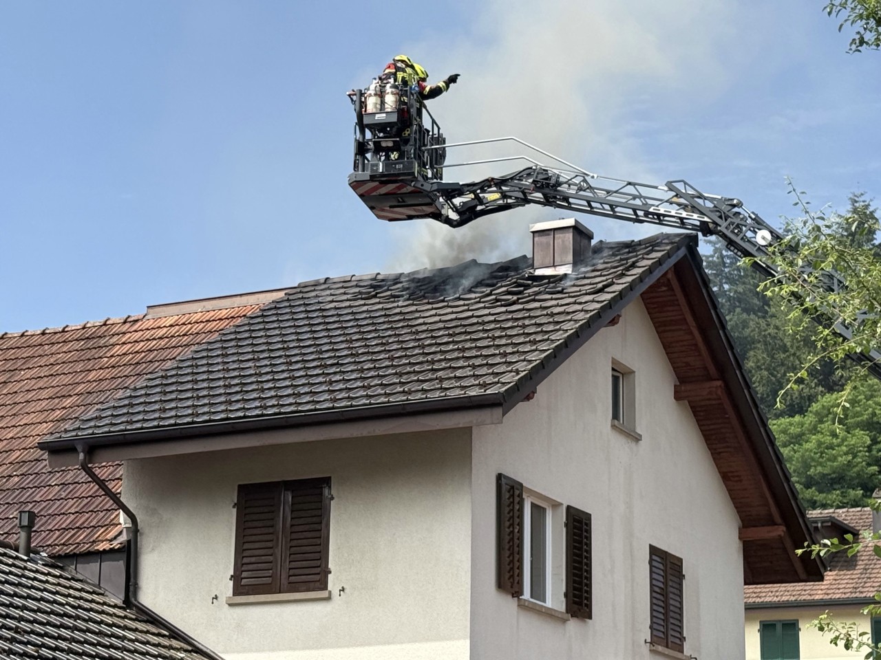 Haus, bei welchem es aus dem Dach raucht. Feuerwehr auf Drehleiter vor Ort.