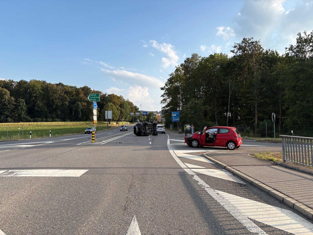 Roter Kleinwagen stark beschädigt und zweites Fahrzeug, welches auf der Seite liegt auf Strasse.