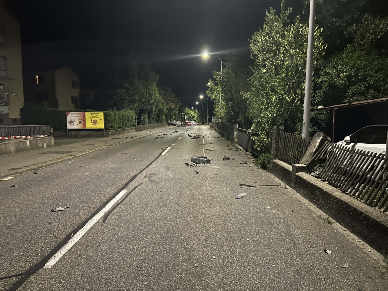 Strasse auf welcher diverse Teile verstreut sind. Auto liegt auf dem Dach.
