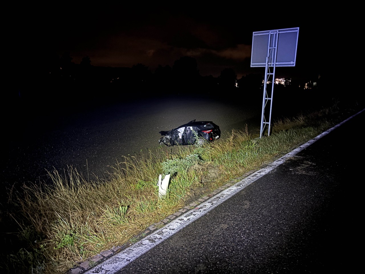 Stark beschädigtes, schwarzes Fahrzeug auf einem Acker neben der Fahrbahn.