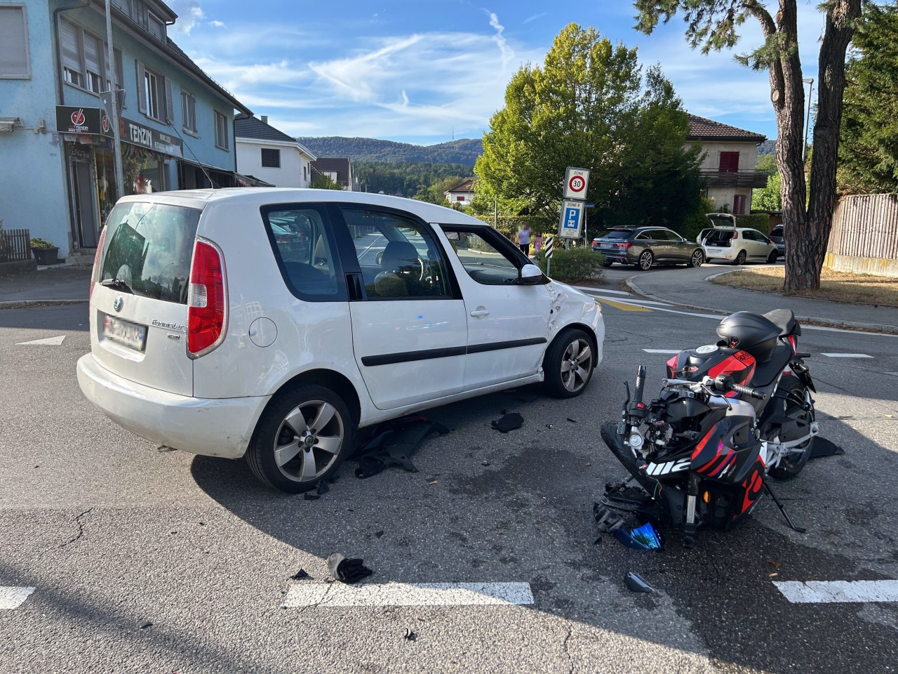 Weisses Auto, welches an der Seite beschädigt ist. Zudem beschädigtes Motorrad am Boden.