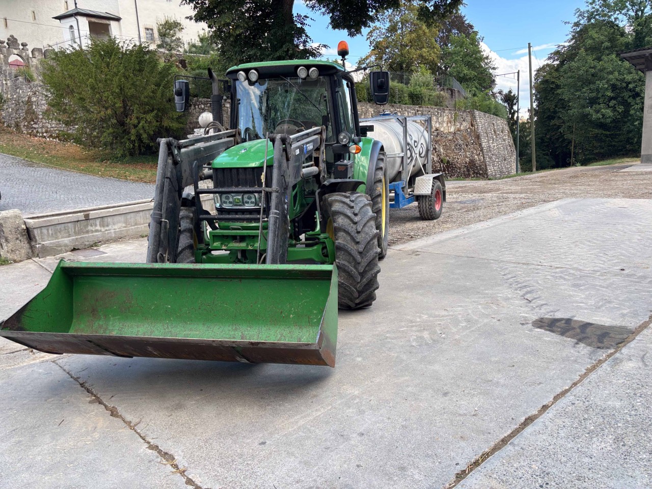 Grüner Traktor mit einem Frontlader und einem Anhänger.