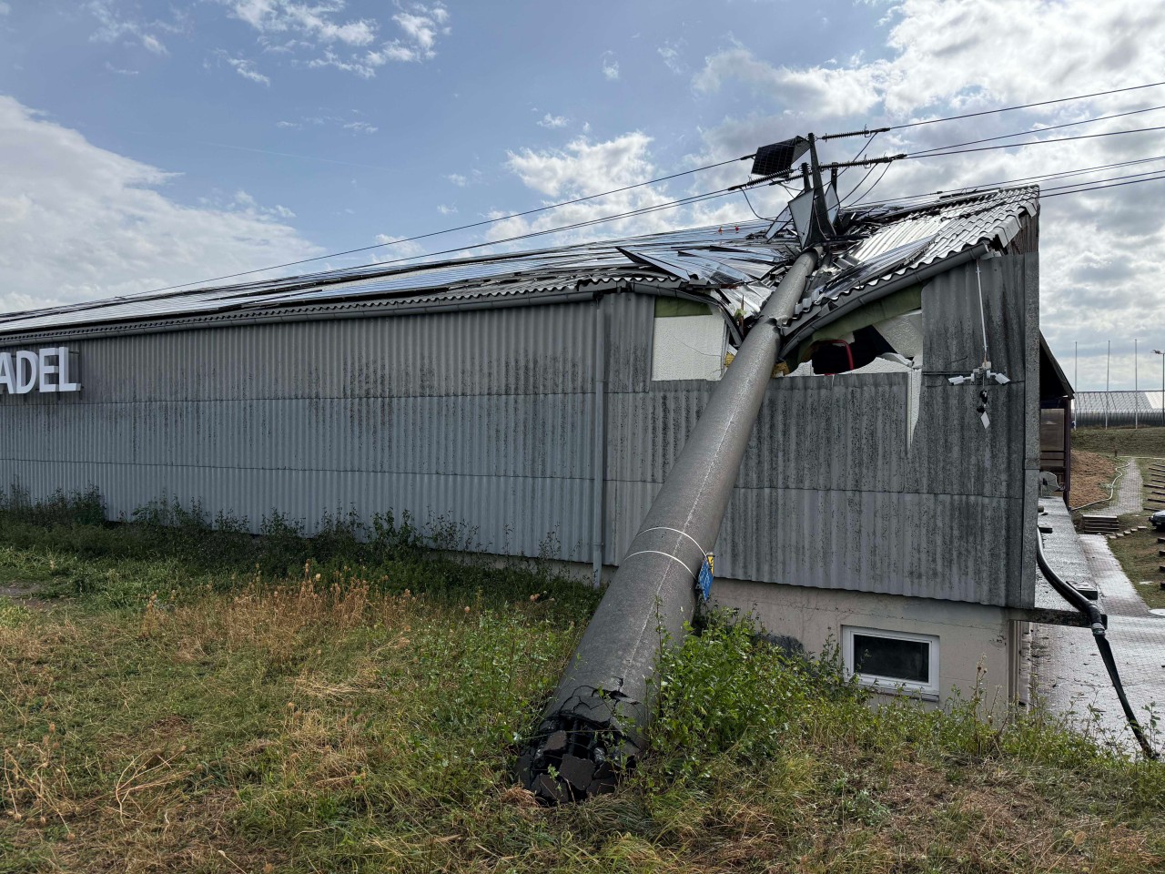 Umgestürzter Betonmast auf Gebäudedach.