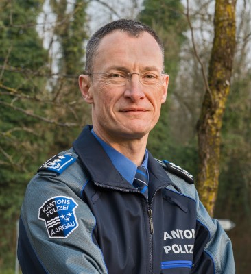Mann mit Uniform der Kantonspolizei Aargau steht am Waldrand.