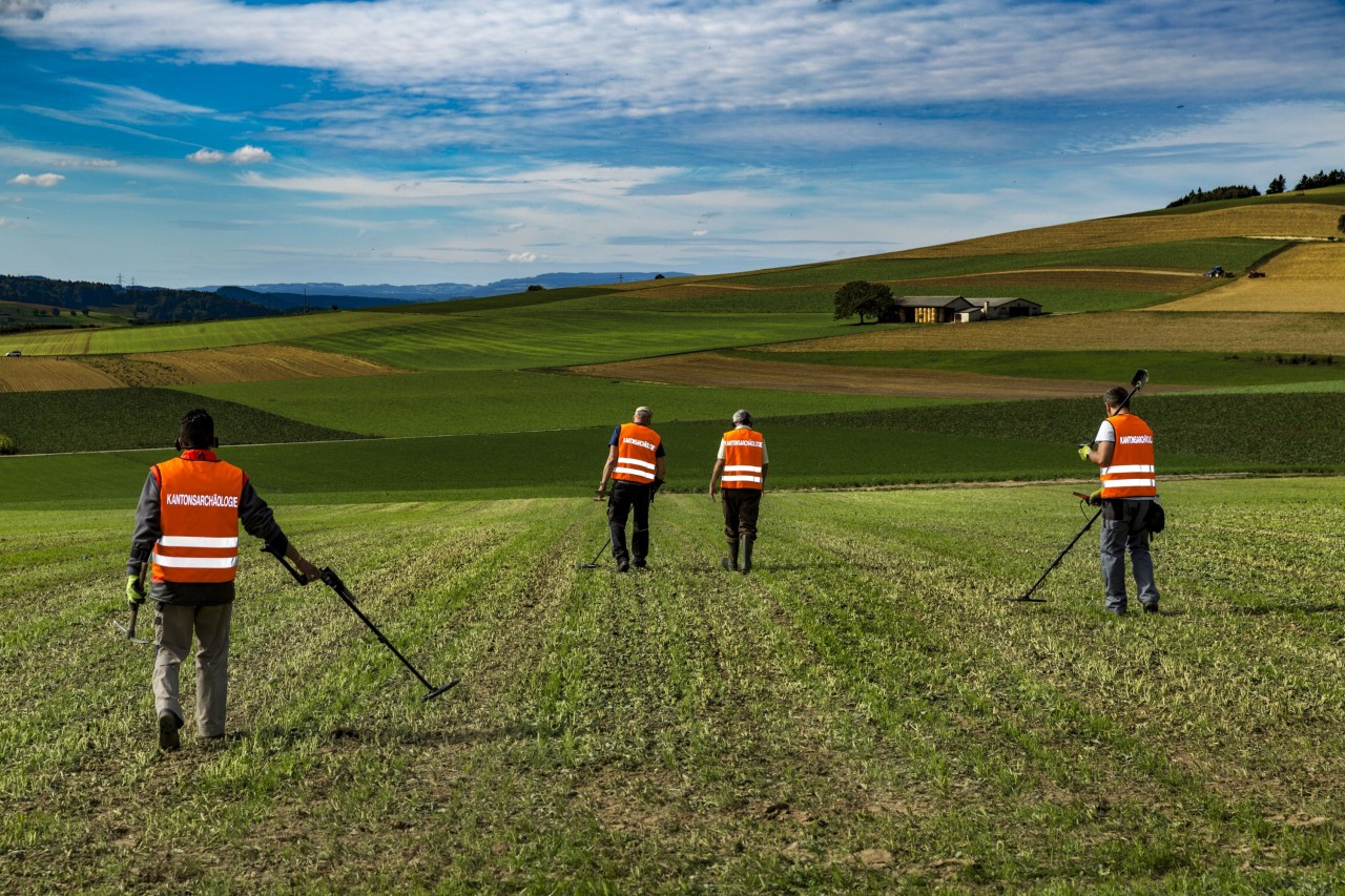 Vier Freiwillige mit einem Metalldetektor auf einem Feld im Einsatz.