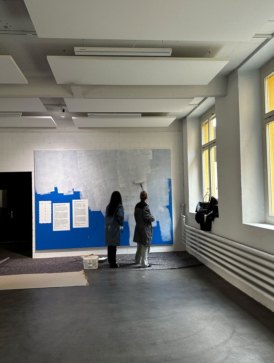 Zwei Personen bemalen eine blaue Wand weiss.