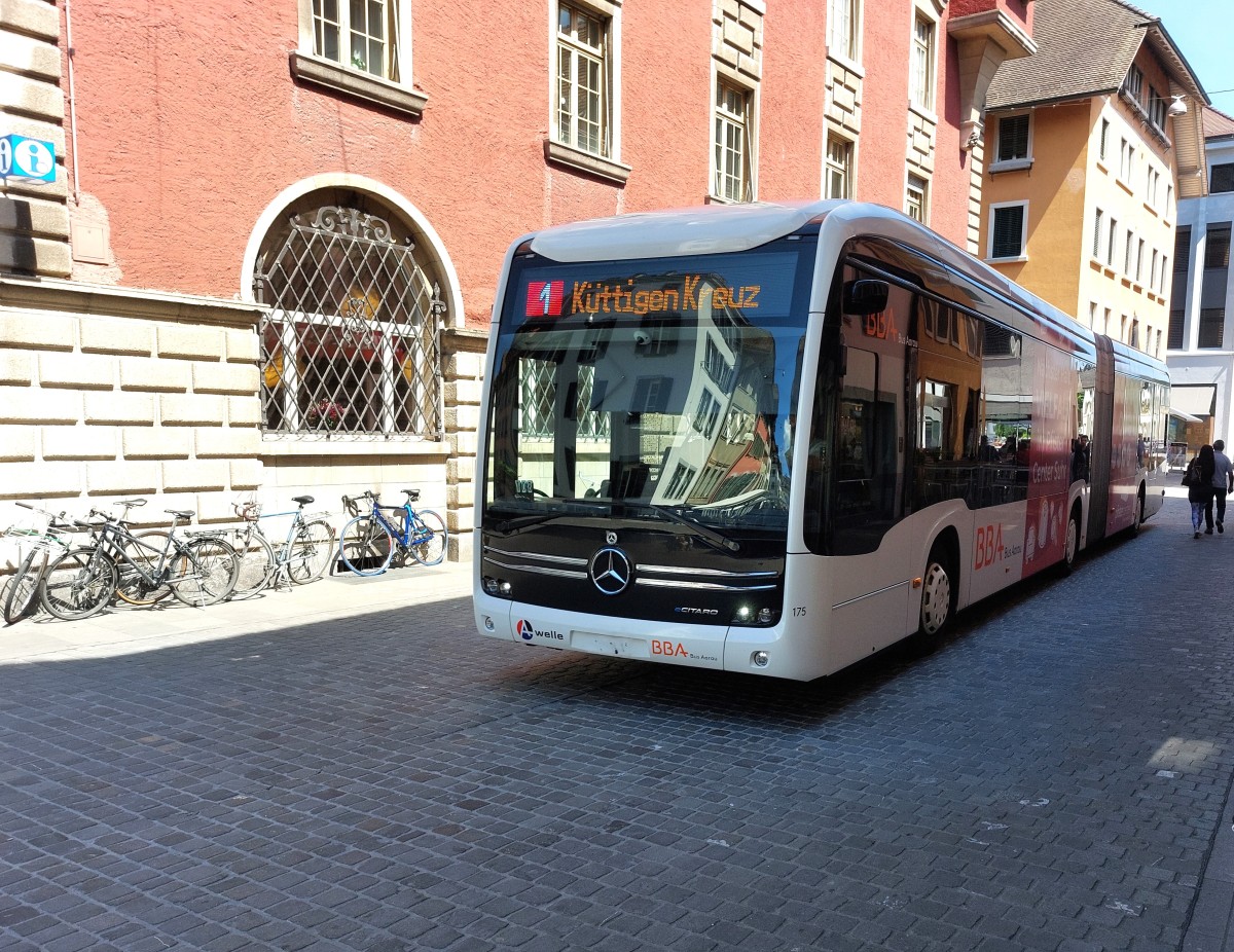 Symbolbild zur Medienmitteilung zum Thema Fahrplan.Ein Bus der Linie 1  nach Küttigen Kreuz fährt durch eine historische Straße mit Fahrrädern und Passanten.