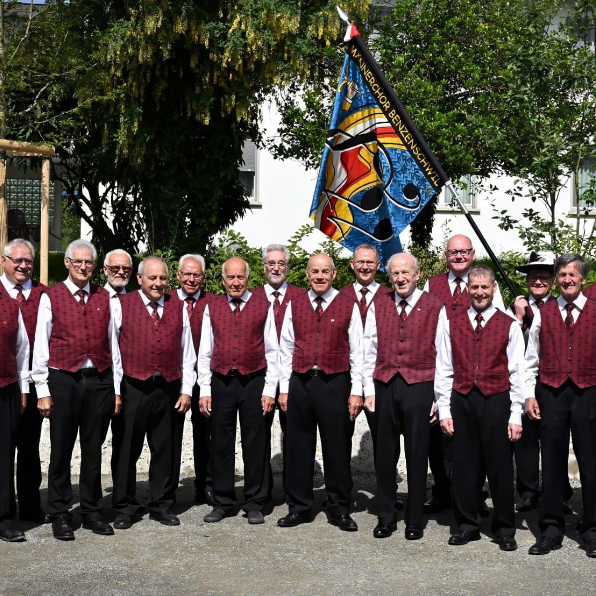 Eine ältere Männergruppe stehen aufgereiht in Choruniform im Grünen.