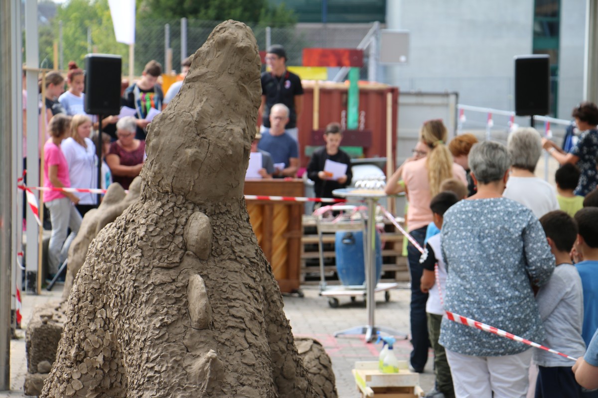 Fokus auf Lehmfigur. Im Hintergrund sieht man Ausstellungsbesucher.