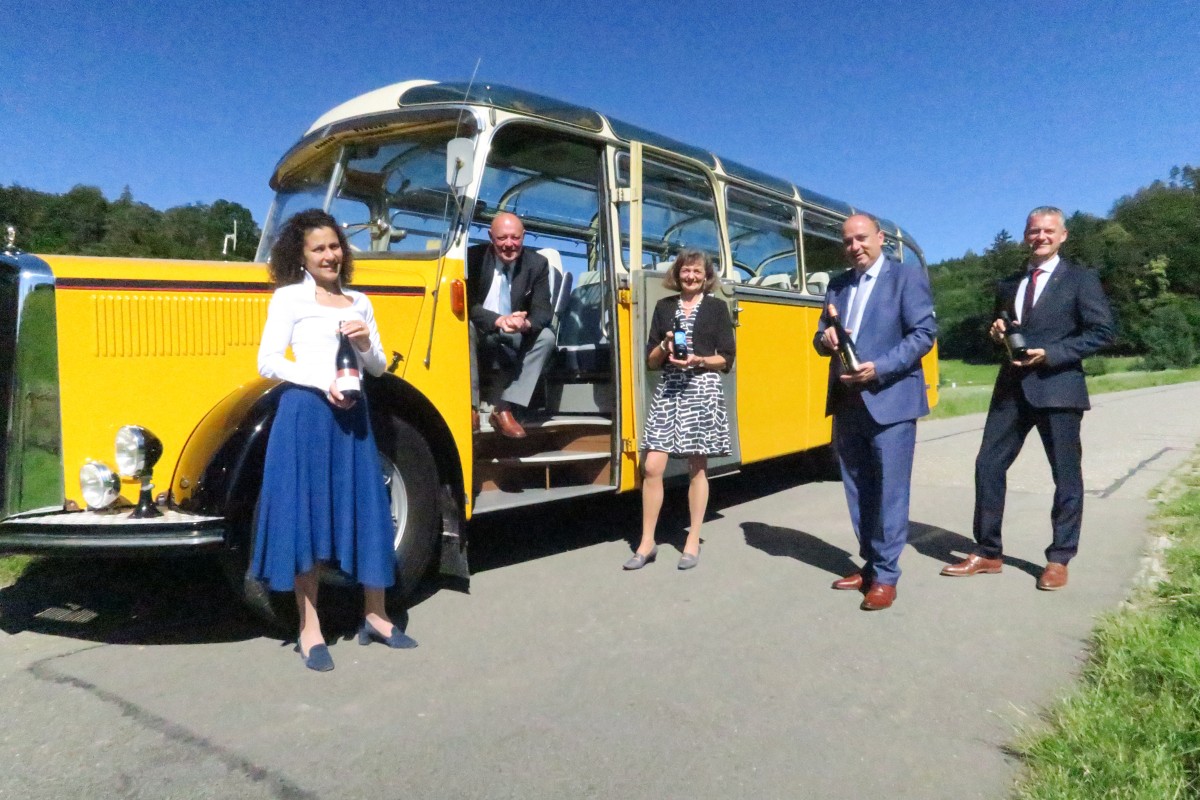 Mehrere Personen stehen mit den Staatsweinen vor einem alten Postauto