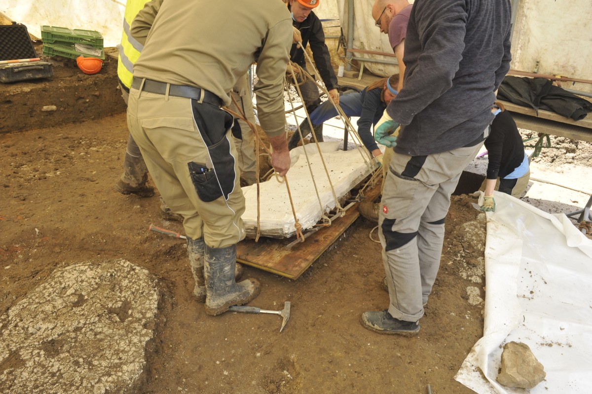 Mehrere Personen legen die Wand mit Seilen auf eine Holzplatte