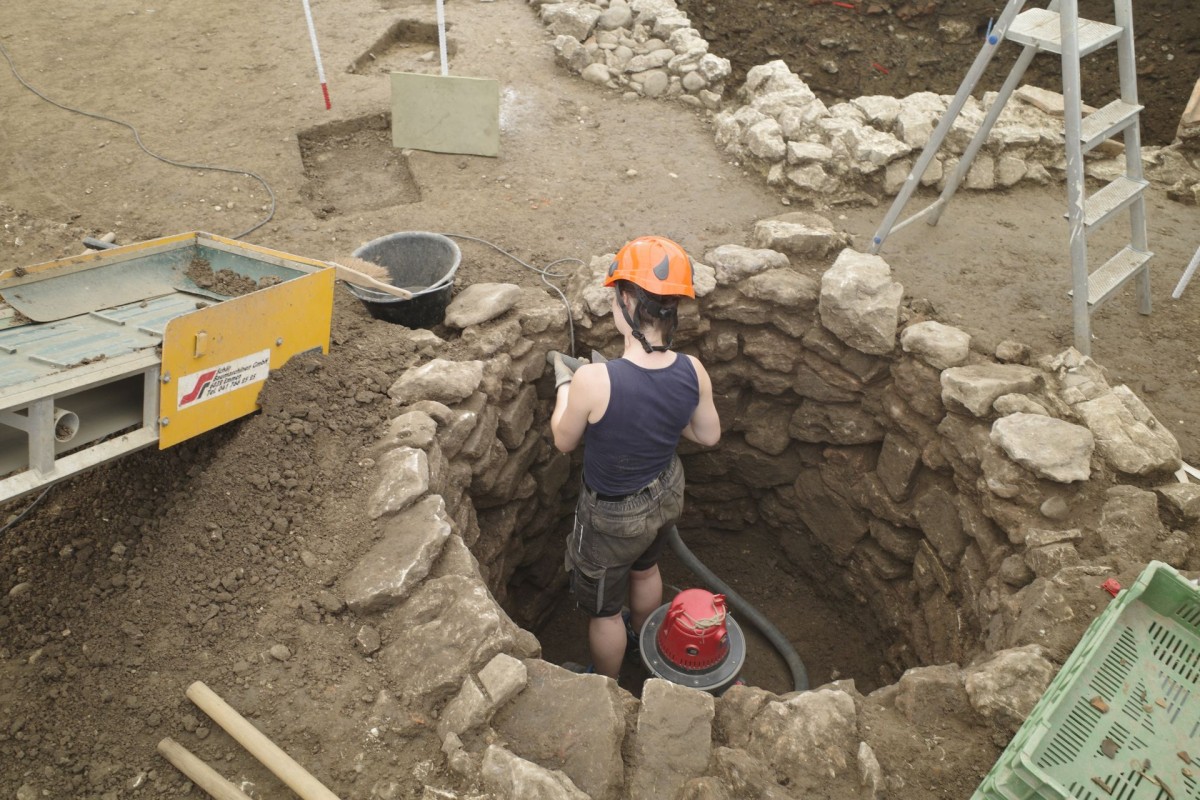 Frau mit einem orangen Schutzhelm arbeitet in einem kreisrunden Schacht.
