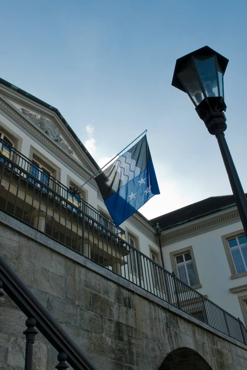 Die Vorder-/Nordseite des Regierungsgebäudes aus der Froschperspektive fotografiert, im Fokus die Aargauer Fahne und eine Strassenlampe