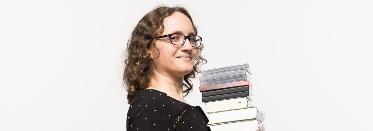 Frau trägt einen Stapel Bücher.