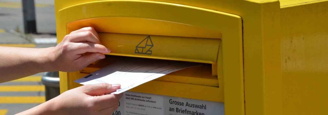 Eine Person wirft ein Abstimmungscouvert in einen gelben Briefkasten