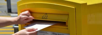 Eine Person wirft ein Abstimmungscouvert in einen gelben Briefkasten