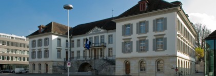 Fotografie des Regierungsgebäudes. Altehrwürdiges Gebäude in Hufeisenform mit einem Balkon in der Mitte mit Aargauer Flagge.