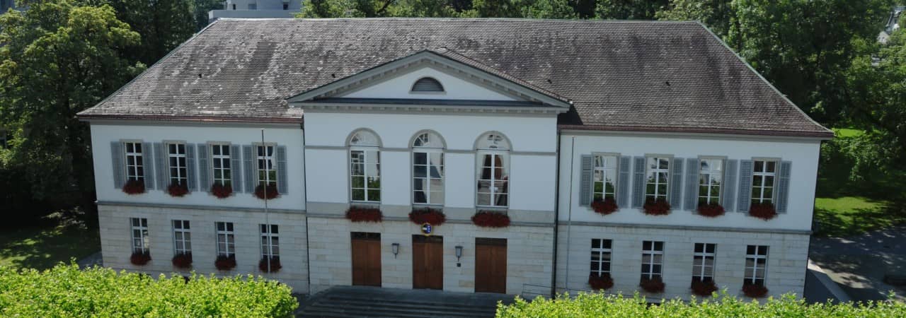 Luftaufnahme vom weissen Grossratsgebäude mit flankierendem Grün rundherum. 