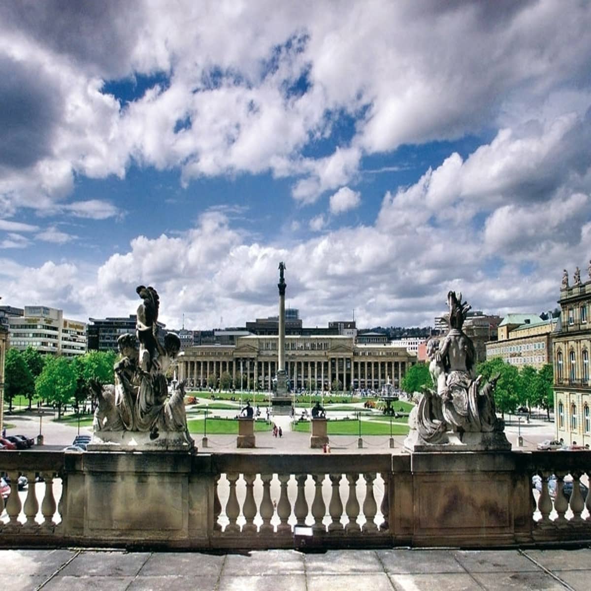 Der Schlossplatz ist ein rundes Gelände mit Grünflächen die von zum Zentrum führenden Wegen unterbrochen sind. In der Mitte steht eine hohe Säule