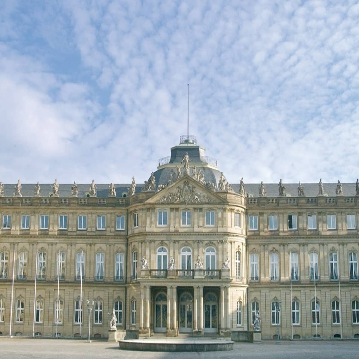 Die Frontansicht des Neuen Schloss: Es ist ein langes Gebäude mit einem dominanten Eingangsbereich.