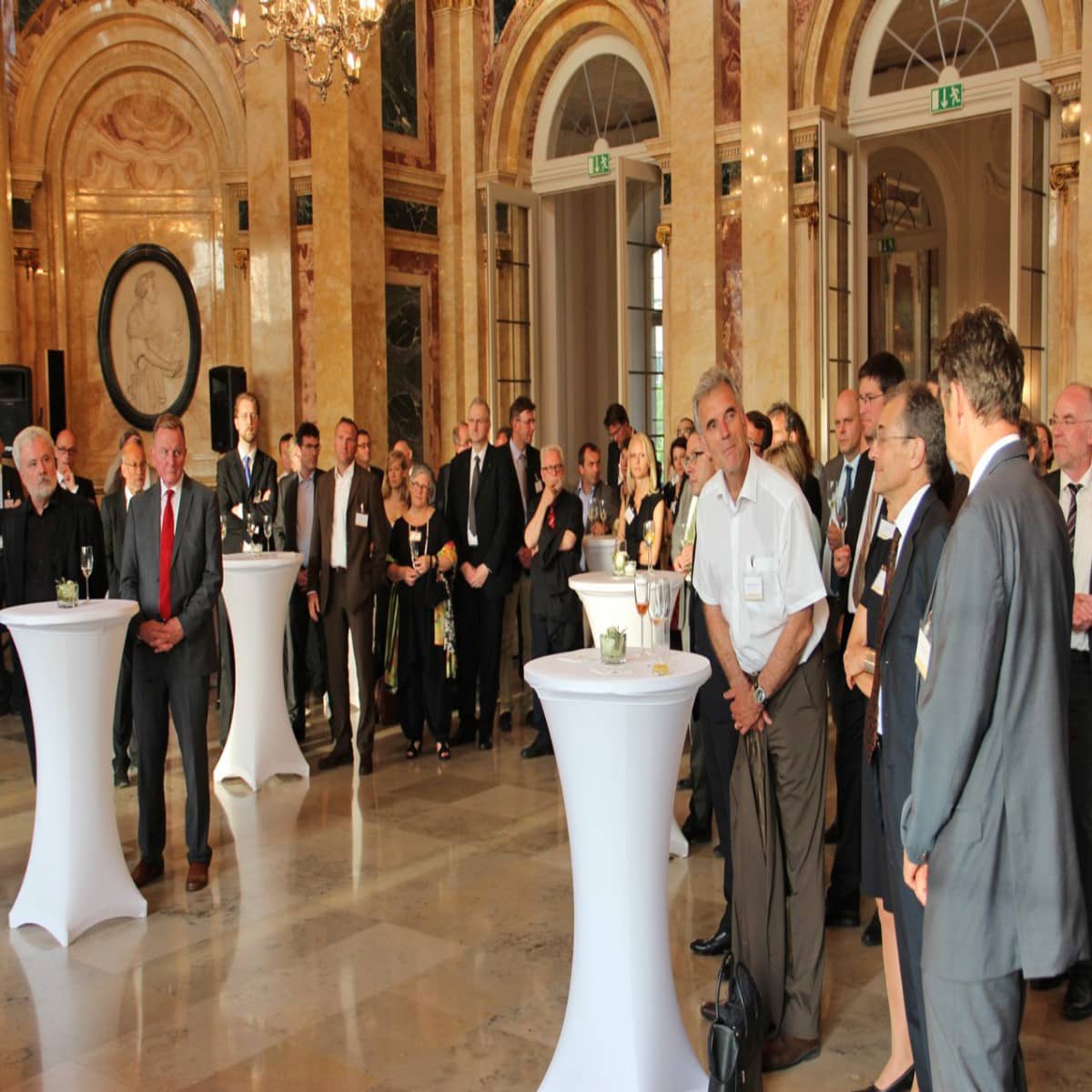 Personen an Tischen stehend in Saal