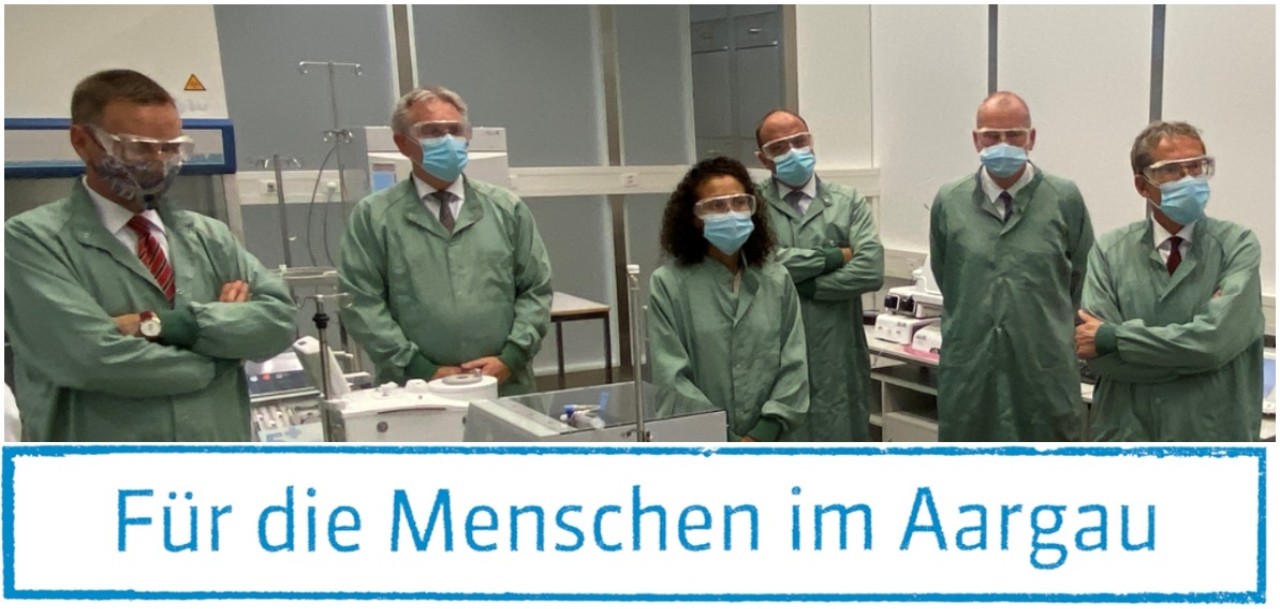 Regierungsmitglieder und Staatsschreiberin Vincenza Trivigno in Schutzanzügen in einem Labor.