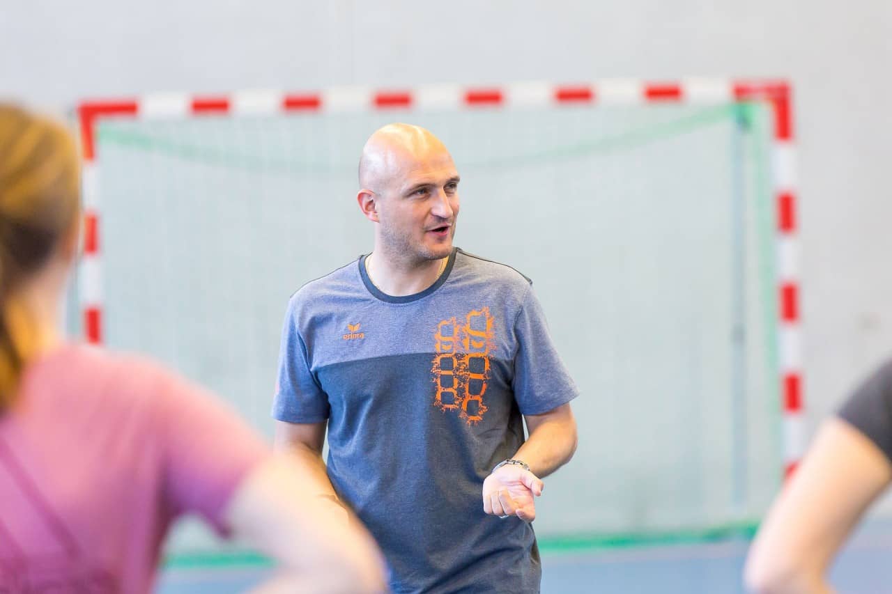 Der Kursleiter steht vor der Gruppe und gibt Erläuterungen zu einer Sportlektion.